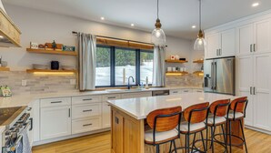 A modern kitchen with white cabinets, a central island with bar stools, a stainless steel refrigerator, and pendant lighting. - Luxe Mountain Home w/ Chef’s Kitchen & Okemo Views (Ludlow)
