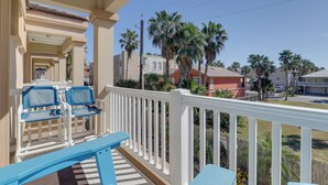 Een balkon met blauwe stoelen en een witte reling, met uitzicht op een woongebied met palmbomen en huizen.