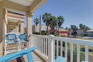A balcony with blue chairs and a white railing overlooking a residential area with palm trees and houses. - Steps to Pool & Beach! South Padre Island Getaway (South Padre Island)