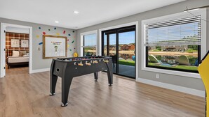 A room with a foosball table, a bed, and a window with a view of a building and a body of water. - *NEW*Private Chef-Family Friendly-Beach-Arcade Games-WI Dells (New Lisbon)