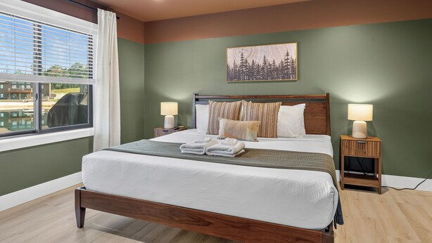 A hotel room with a large bed, two bedside lamps, a view of a building outside, and a painting on the wall. - *NEW*Private Chef-Family Friendly-Beach-Arcade Games-WI Dells (New Lisbon)