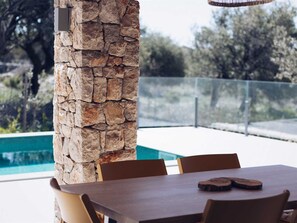 An outdoor dining area with a stone pillar, a pool, and a view of trees. - Experience Villa Kadila – Heated Pool & Sauna in a Timeless Olive Grove (Jakišnica)