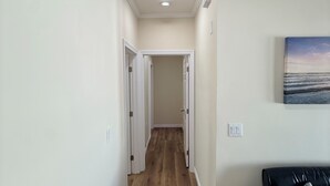 A hallway with wooden flooring, white walls, and a black couch with a pillow. - Modern 3BR LA Home near Downtown LA, Perfect for Families and Large Groups (Los Angeles)