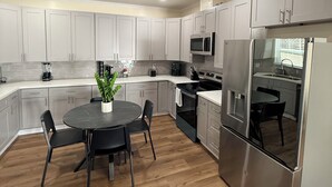 A modern kitchen with grey cabinets, stainless steel appliances, a round dining table with chairs, and a potted plant. - Modern 3BR LA Home near Downtown LA, Perfect for Families and Large Groups (Los Angeles)