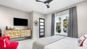 A hotel room with a bed, a red chair, a TV, a cabinet, and a window with curtains. - Presidio Hotel - 2nd Floor (Johnson City)