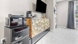 A modern hotel room with a flat-screen TV mounted on the wall, a minibar, a wooden cabinet with circular patterns, and a view of the outdoors through a window. - Presidio Hotel - 2nd Floor (Johnson City)