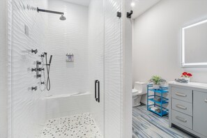 A modern bathroom with a glass-enclosed shower, a white tiled wall, a blue storage unit, and a white sink with a mirror above it. - Presidio Hotel - 1st Floor (Johnson City)
