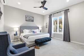 Ein Schlafzimmer mit Bett, Stuhl, Bank, Deckenventilator und einem Fenster mit Vorhängen.