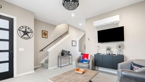 A modern living room with a staircase, a flat-screen TV, a coffee table, and a sofa. - Presidio Hotel - 2 Story Suite (Johnson City)