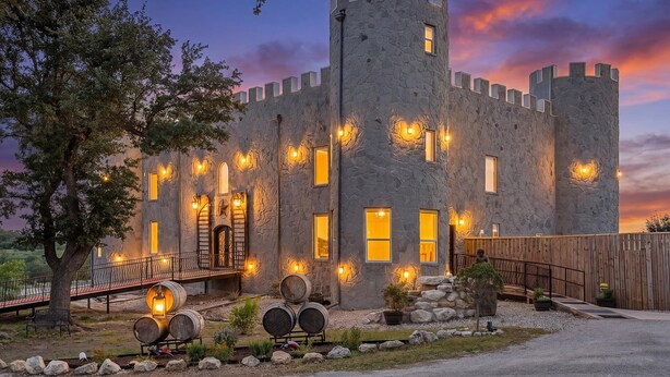 A stone castle-style building with multiple windows and a wooden fence. - Presidio Hotel - 2 Story Suite (Johnson City)