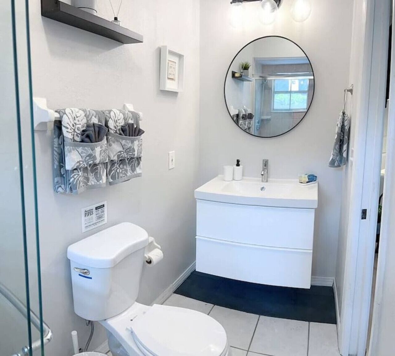 A modern bathroom with a toilet, sink, and mirror. There are storage baskets on the wall and a framed picture above the mirror.