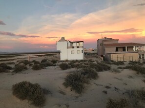 Wüstenlandschaft mit zwei Gebäuden, eines mit Kuppel und das andere mit Balkon, unter einem Sonnenuntergangshimmel.