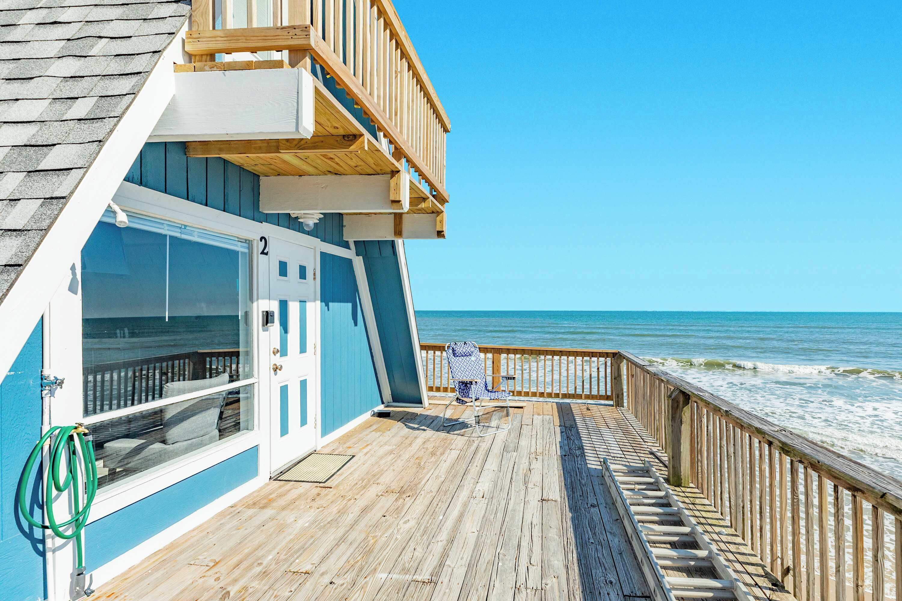 A wooden deck with a view of the ocean, a door labeled '2', and a chair on the deck.