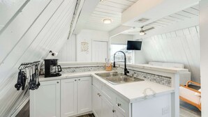 A compact kitchen with white cabinetry, a built-in sink, and a coffee maker. - Iconic A Frame Directly Over The Surfside Waves (Surfside Beach)