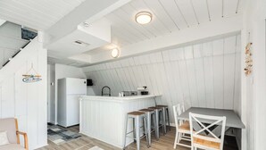 A modern kitchen with a central island, bar stools, and a dining table with chairs. - Iconic A Frame Directly Over The Surfside Waves (Surfside Beach)