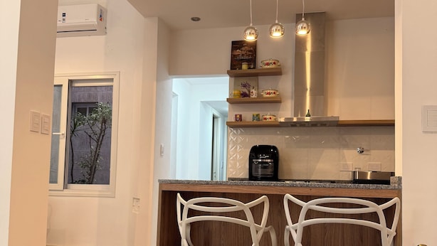 Una cocina moderna con dos taburetes blancos, suelo de madera e iluminación colgante.