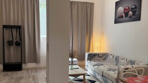Una sala de estar moderna con un sofá, una mesa de comedor y una mesa de centro. Hay una silla colgante negra y una mesita con un florero. La habitación tiene un ventanal con cortinas.
