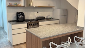 Una cocina moderna con una isla central, taburetes blancos estilo barra, horno empotrado y refrigerador.