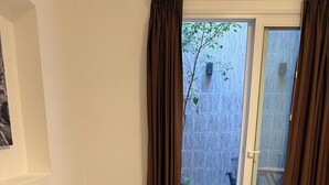 Un dormitorio con cama, almohadas, una mesita de noche, una lámpara y un ventanal corredero que da a un espacio exterior con una silla y una mesa.