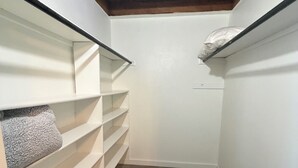 Een smalle inloopkast met houten vloer, witte wanden en inbouwplanken.