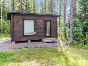 A small wooden cabin with a large window and a door, surrounded by trees.