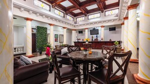 A spacious, elegantly furnished lounge with a high ceiling, large windows, and a central seating area. - Hotel in San Jose Hotel Majestad (San Jose)