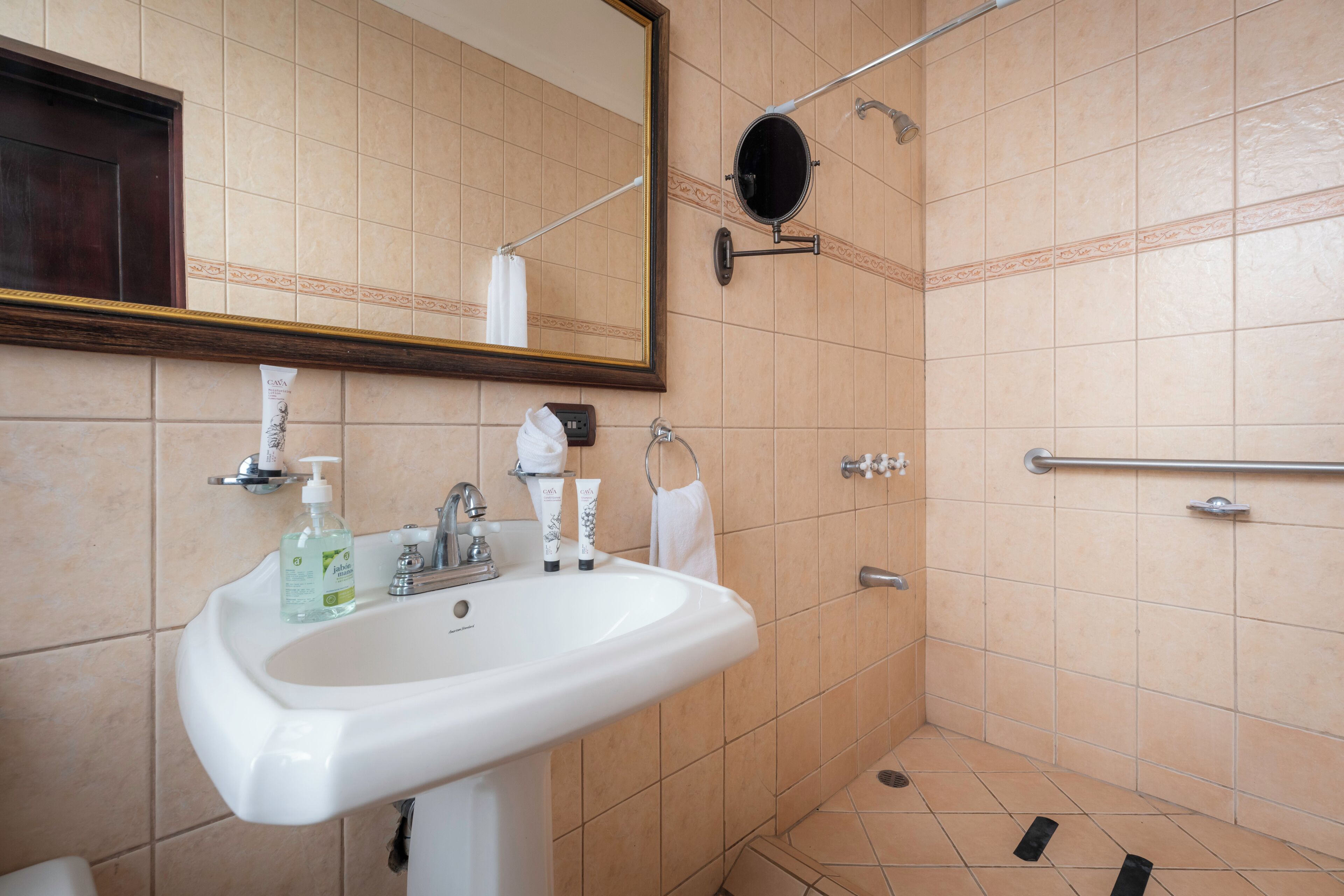 A bathroom with a sink, mirror, shower, and tiled walls.