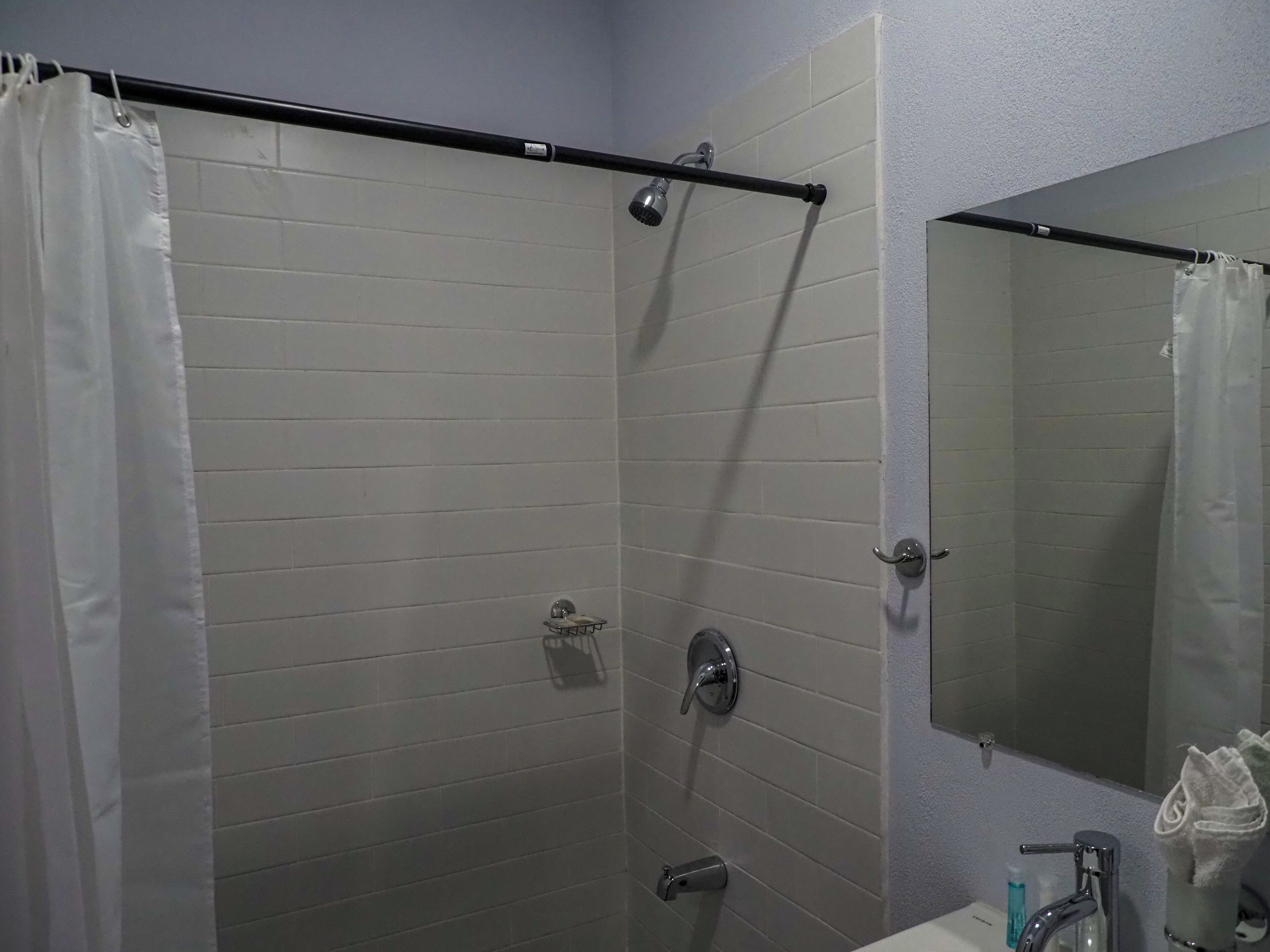 A shower with a curtain, a handheld showerhead, a towel rack, and a mirror.