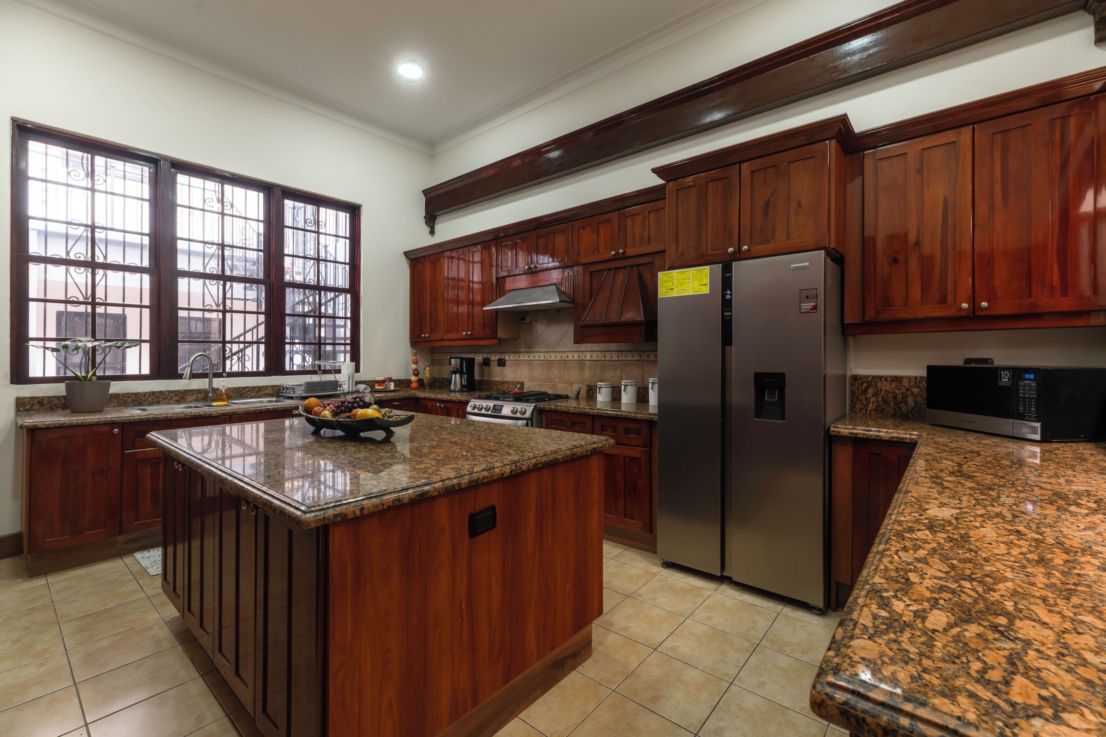 A kitchen with wooden cabinets, a granite countertop, a stainless steel refrigerator, and a gas stove.