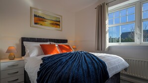 Una camera da letto con un letto, comodini, una lampada, un quadro e una finestra con tende.