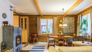 A cozy cabin interior with a stone fireplace, wooden walls, a dining area, and a large window with curtains. - Vacation home Metsis by Interhome (Nurmes)