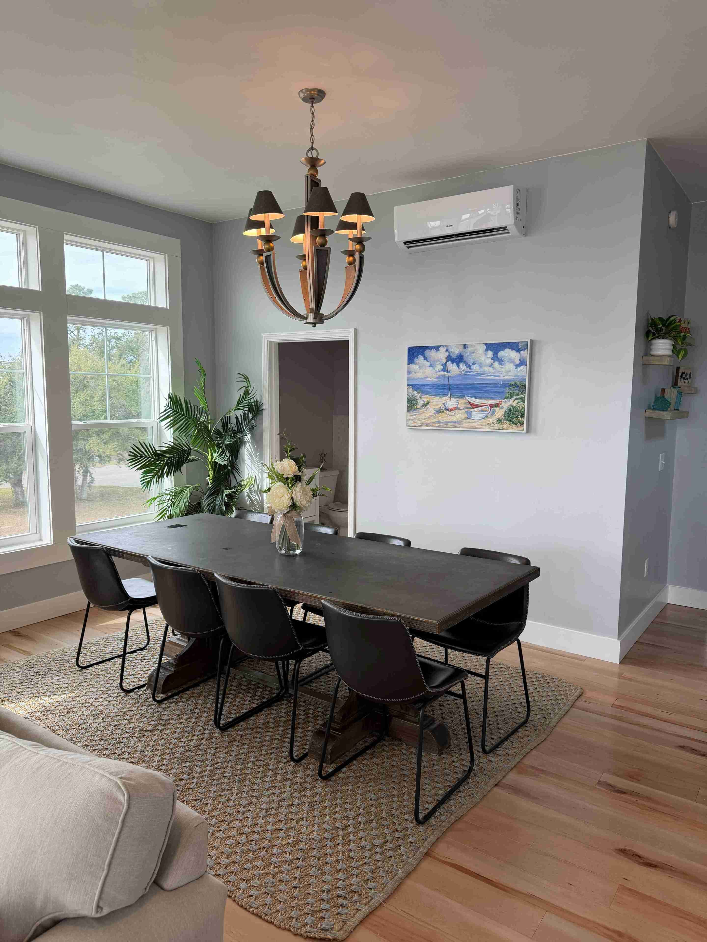 A dining area with a dark wooden table, black chairs, a chandelier, and a painting of a beach scene.
