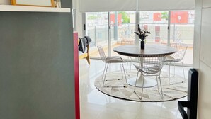 A modern dining area with a round table and wire chairs, a framed picture on the wall, and a view of the outside through large windows.