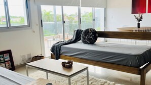 A modern bedroom with a bed, a small table, a rug, and a view of the outdoors.