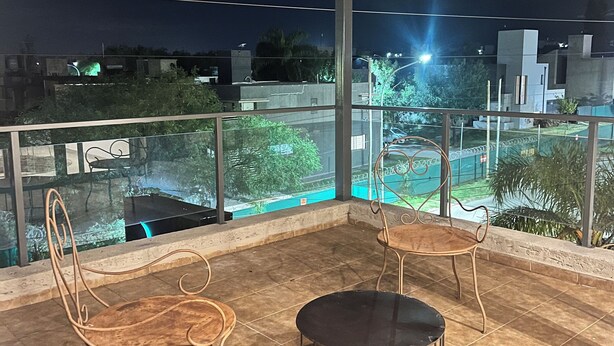An outdoor terrace with two wooden chairs and a table, surrounded by a glass railing.