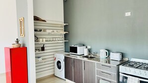 A compact kitchen with a red refrigerator, a washing machine, a microwave, a toaster, and a gas stove.