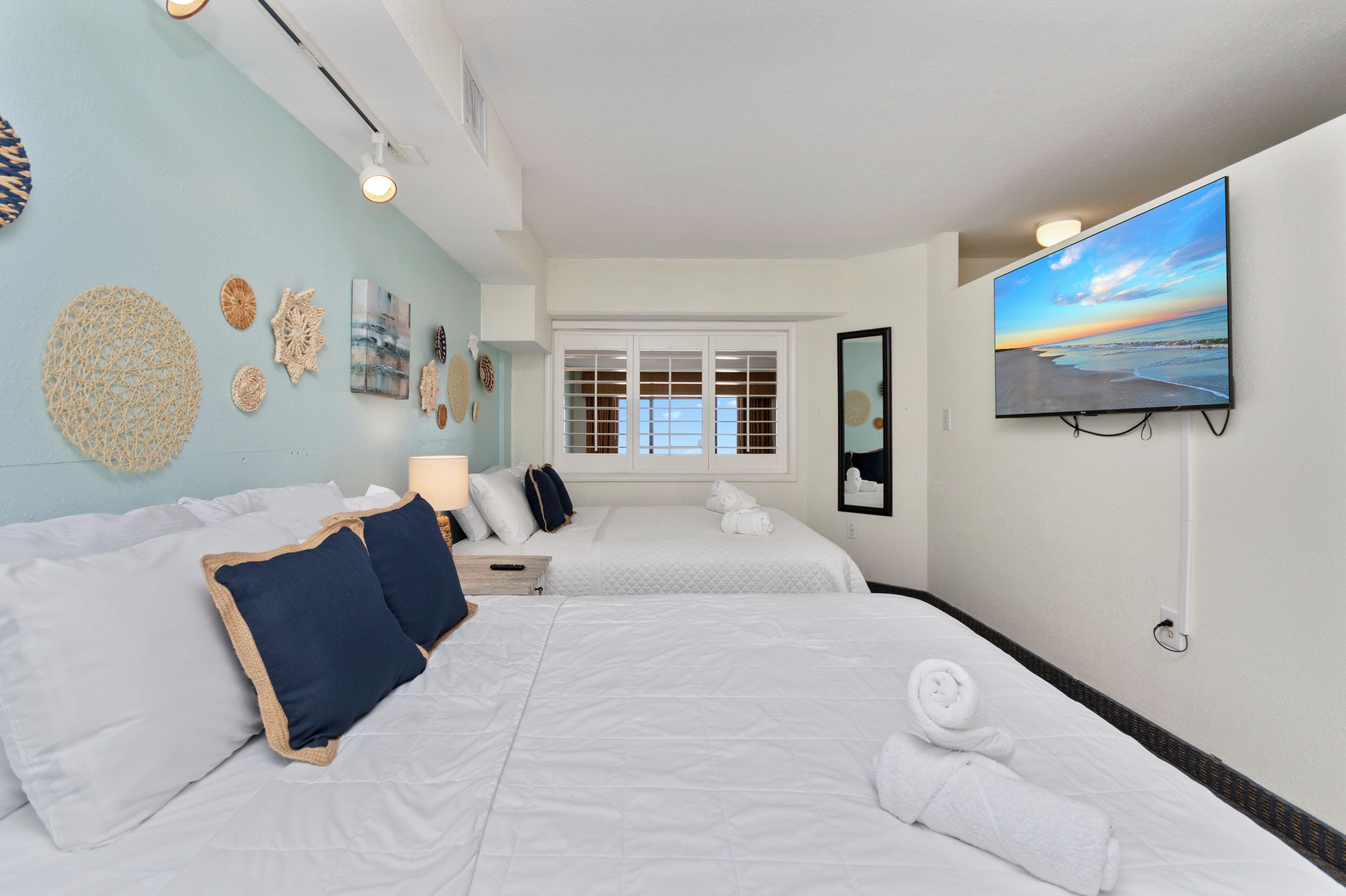 A hotel room with two beds, a TV, a window with blinds, and wall decor.
