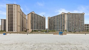 A beachfront hotel with multiple high-rise buildings, sandy beach, and a lifeguard station. - Oceanfront, Pools, Lazy River @ Beach Cove Resort (North Myrtle Beach)