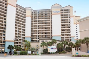 Ein großes Hotel mit mehreren Stockwerken, einem auffälligen Schild mit der Aufschrift 'Beach Cove' und einem Parkplatz mit palmenbestandener Einfahrt.