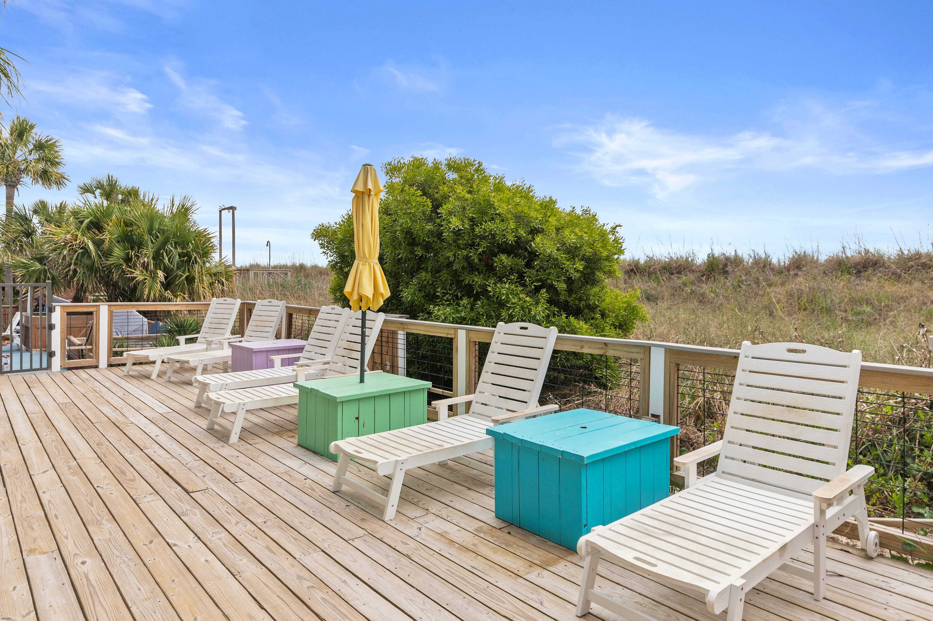 A wooden deck with white lounge chairs and colorful storage boxes.