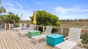 A wooden deck with white lounge chairs and colorful storage boxes.