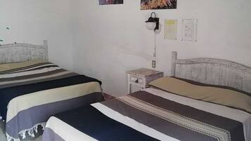A room with two beds, a nightstand, a wall-mounted lamp, and three posters on the wall.