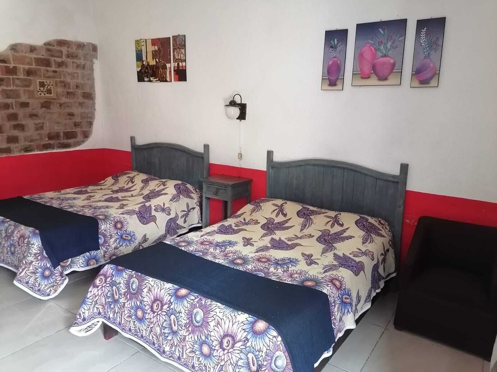 A room with two beds, a brick wall, and three paintings on the wall.
