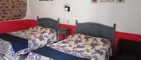 A room with two beds, a brick wall, and three paintings on the wall.