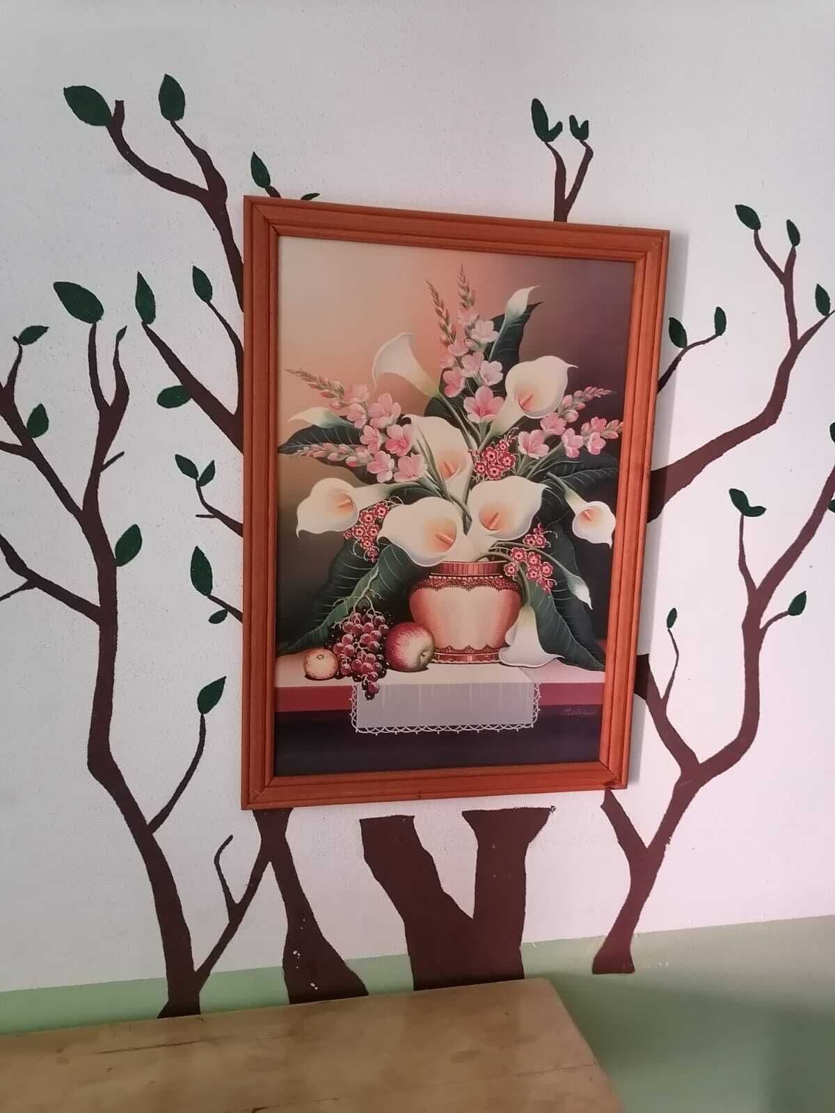 Un cuadro enmarco con flores y frutas sobre una mesa, rodeado de adhesivos murales con forma de árboles.