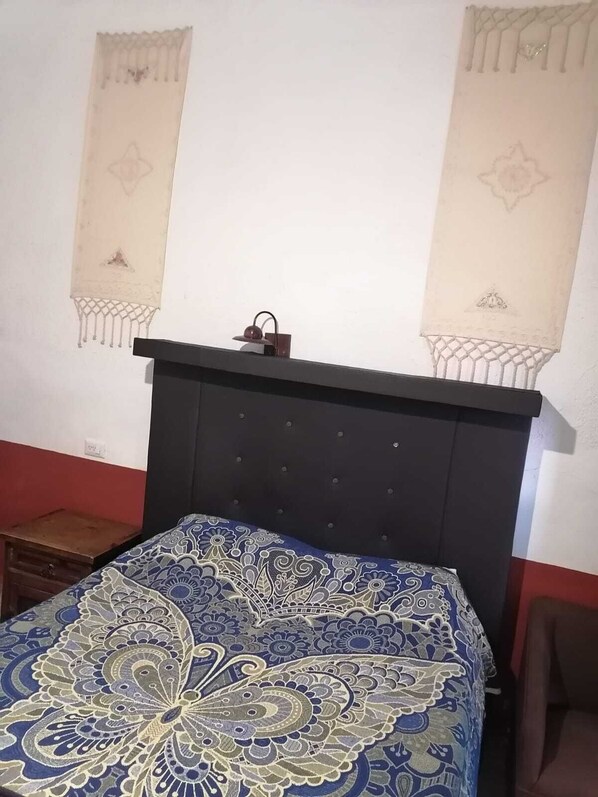 Une chambre à coucher avec une tête de lit sombre, une couvre-lit à motifs et deux décorations murales.