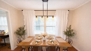 Comedor con mesa de madera, cuatro sillas, una araña y dos plantas en macetas.