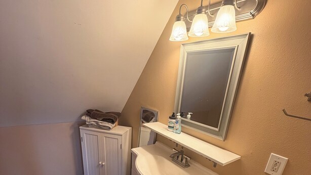 Une salle de bain avec un meuble-lavabo, un miroir et un luminaire placé au-dessus du miroir.