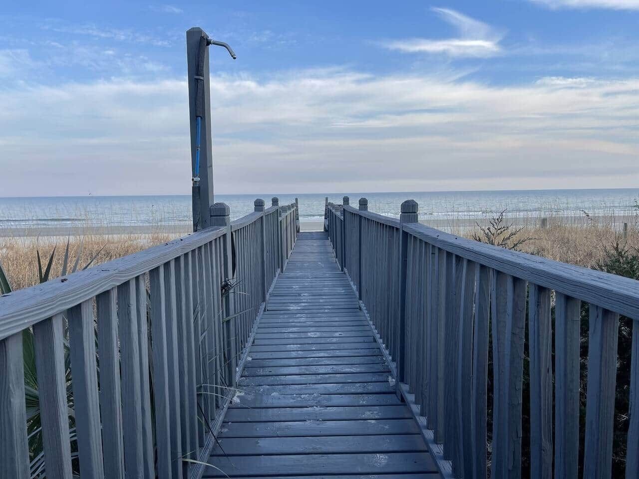 Une promenade en bois menant à la plage, sous un ciel dégagé.