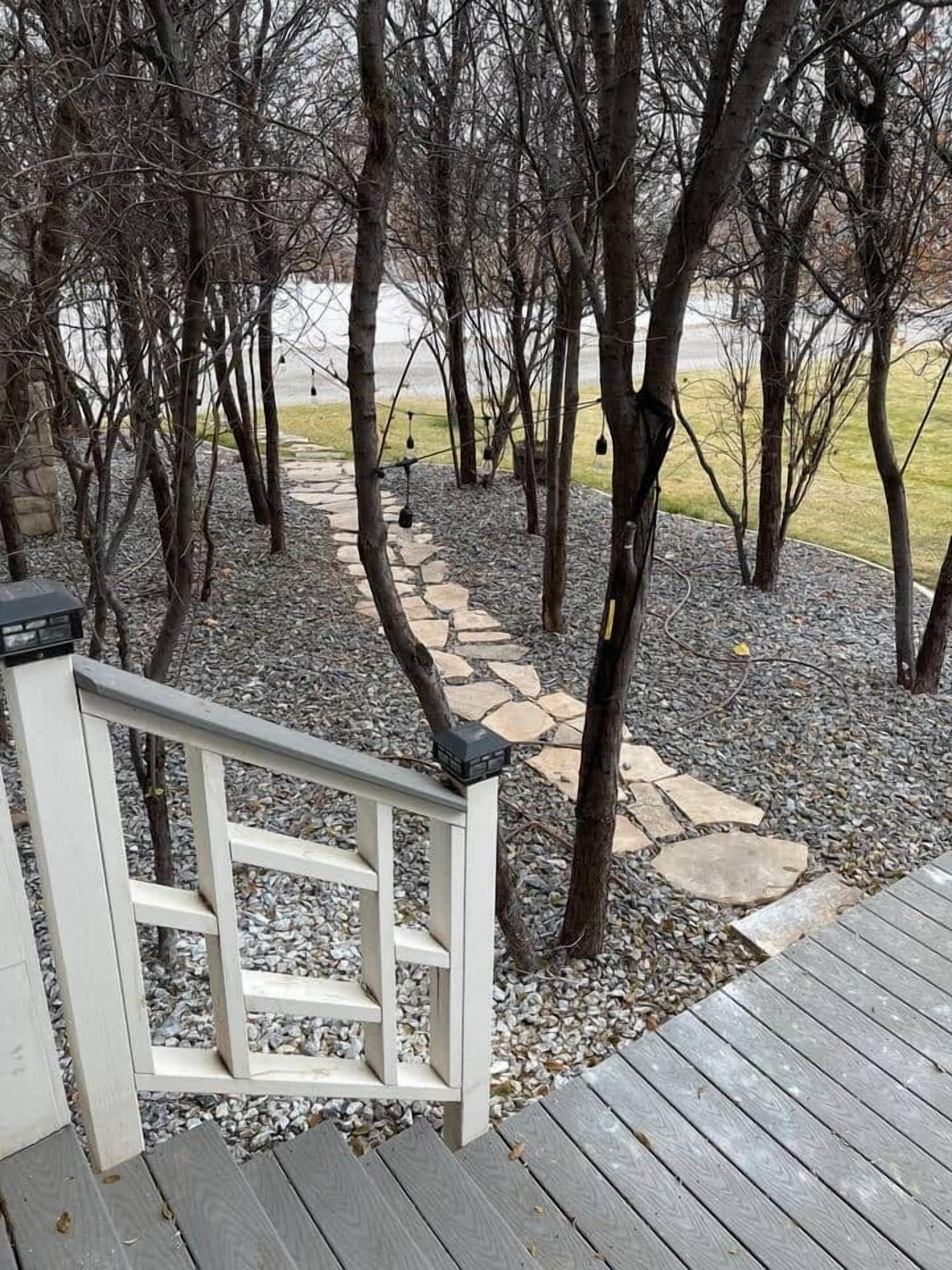 Une terrasse en bois avec un chemin de pierre menant à une rambarde blanche.